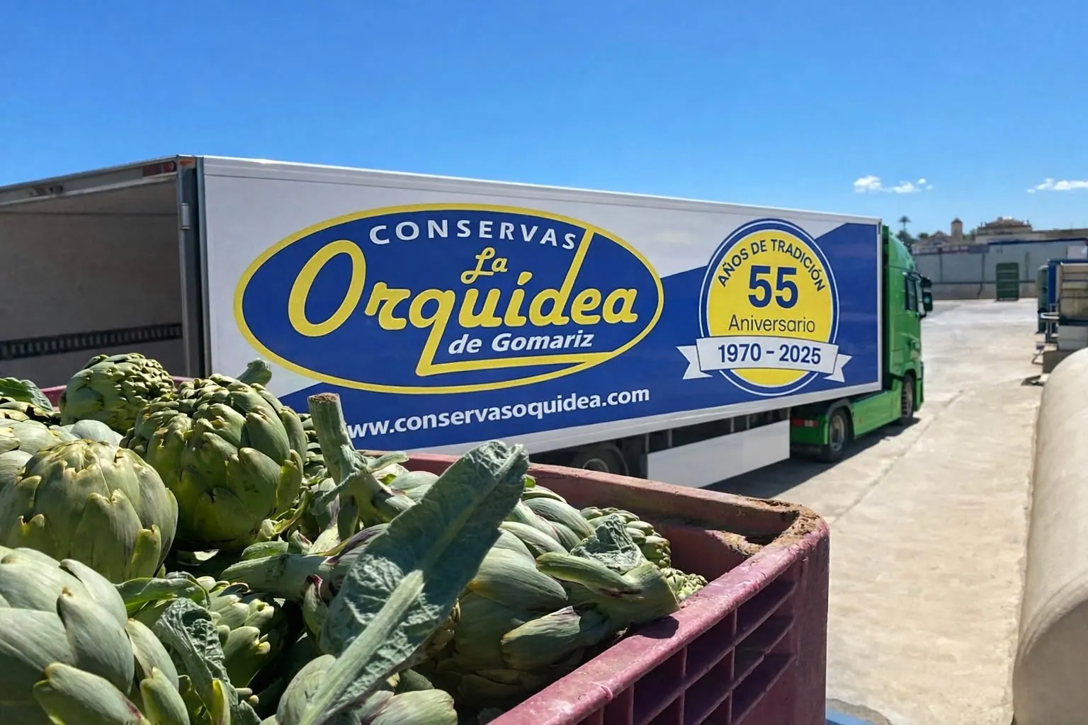 Conservas La Orquídea lorry with the brand logo and the 55th anniversary seal, next to a bin of freshly harvested artichokes